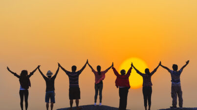 teamwork concept silhouette diversity people show hands high up over head successful partner together at sunset on top rock hill.